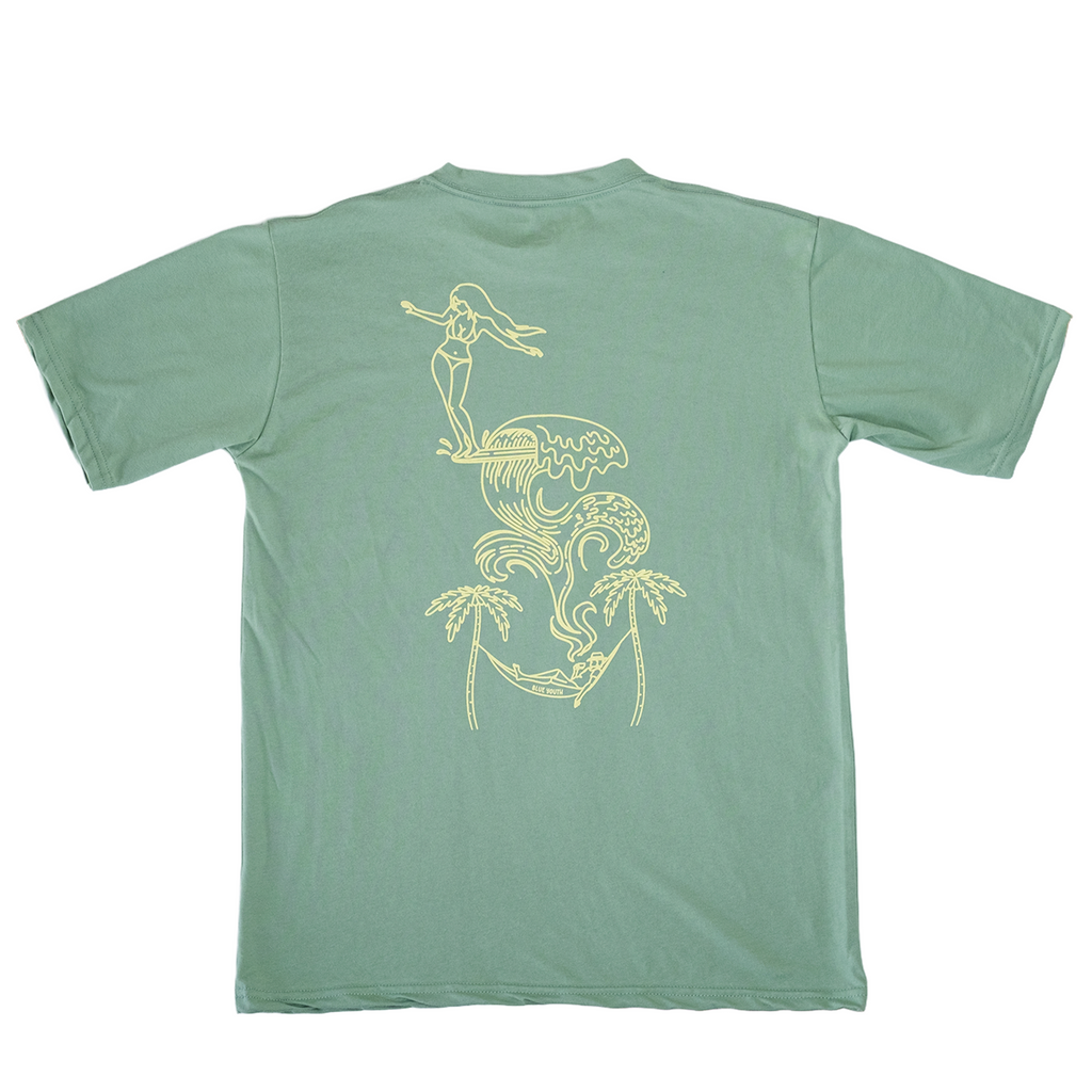 Camiseta verde con arte gráfico de una chica surfeando y un diseño tropical tipo ensueño, parte de la colección Blue Youth.