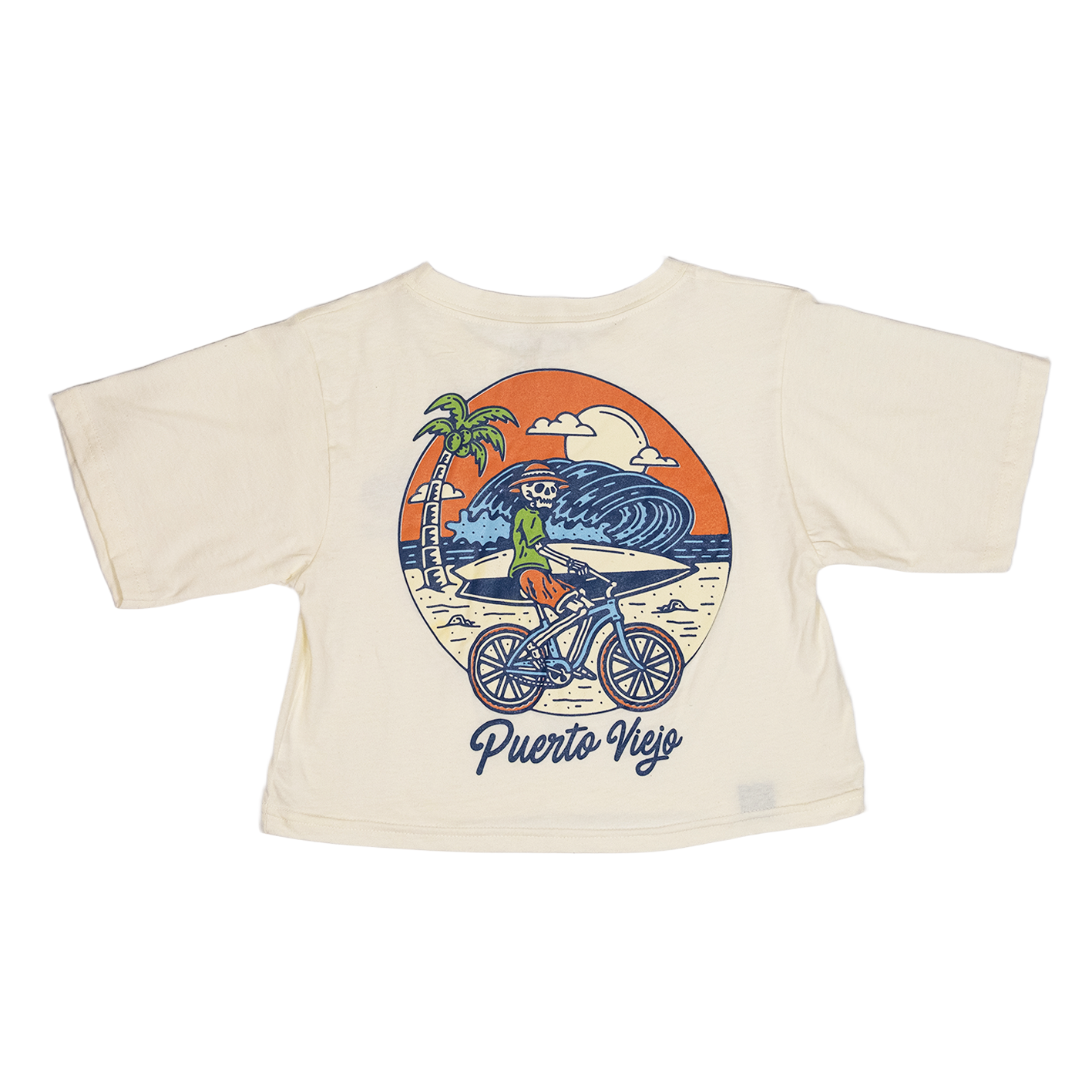 Crop top blanco con ilustración de esqueleto en bicicleta en la playa de Puerto Viejo, con ola gigante y palmera al fondo.

